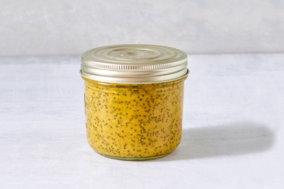 A small container of homemade mustard, yellow with speckles of black and brown mustard seed