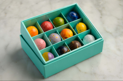 A blue box filled with a dozen unique chocolates in blues, reds, yellows, and browns. Each chocolate is dipped in a jewel-inspired glaze.