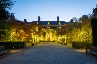 A photograph of the Filoli entrance at dusk. Several lights are placed on the building and surrounding trees giving off a warm glow.
