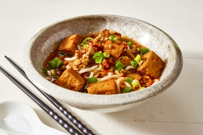 A bowl of Hunan Hot and Sour Noodles: containing noodles, tofu, and other vegetables in a red broth