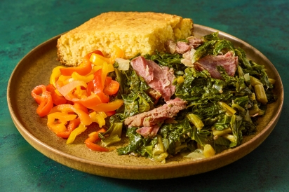 Plate with cornbread, cooked bell peppers, and braised mustard greens topped with meat