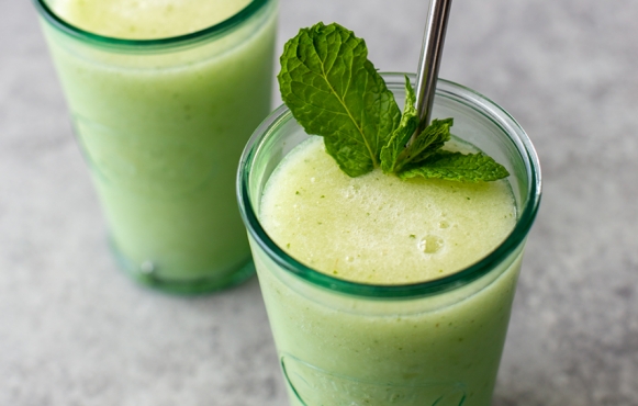 Two Cucumber Pear Mojito Slushies. Both are in glass containers, one has a metal straw, and is topped with fresh mint.