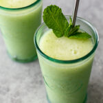 Two Cucumber Pear Mojito Slushies. Both are in glass containers, one has a metal straw, and is topped with fresh mint.